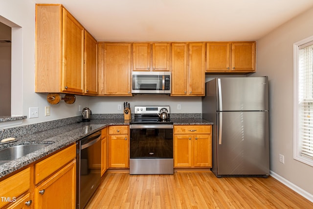 kitchen with stainless steel appliances, dark stone counters, brown cabinets, and light wood-style flooring