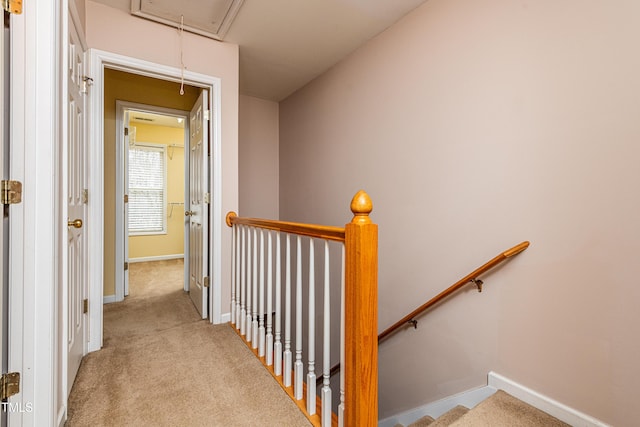 hall featuring carpet, an upstairs landing, attic access, and baseboards