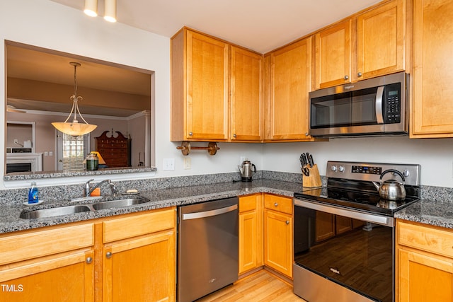 kitchen with light wood-style flooring, a fireplace, a sink, appliances with stainless steel finishes, and dark stone countertops