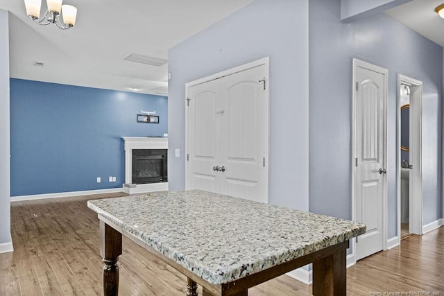 kitchen featuring a chandelier, wood finished floors, baseboards, light countertops, and a glass covered fireplace