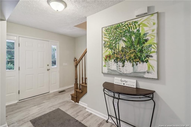 foyer entrance featuring a textured ceiling, wood finished floors, visible vents, baseboards, and stairway