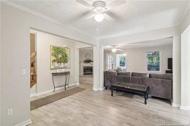 living area with crown molding, a fireplace, ceiling fan, a textured ceiling, and wood finished floors