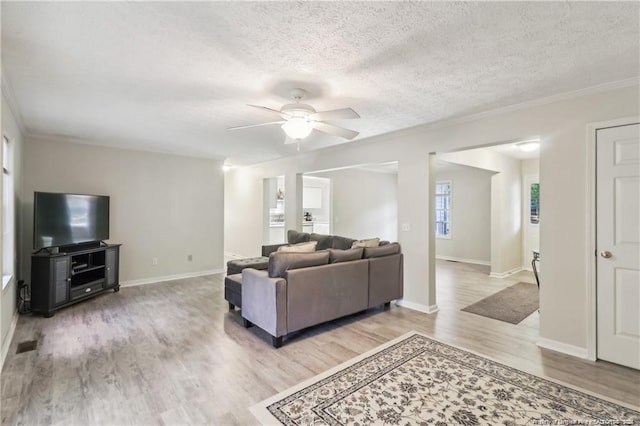 living area featuring visible vents, baseboards, a textured ceiling, and light wood finished floors