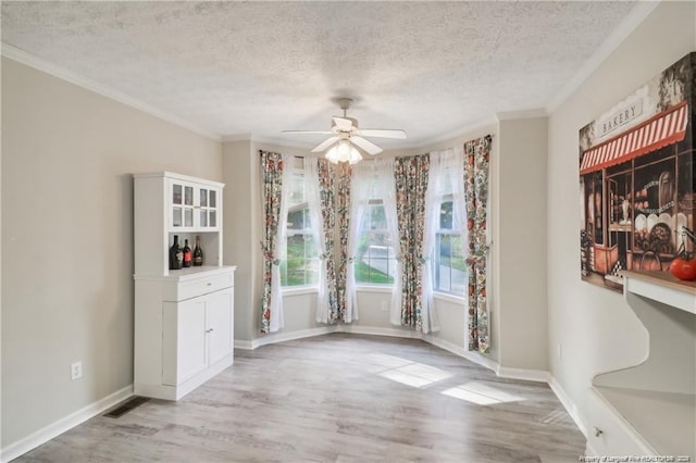 unfurnished dining area with ceiling fan, ornamental molding, light wood-style flooring, and baseboards