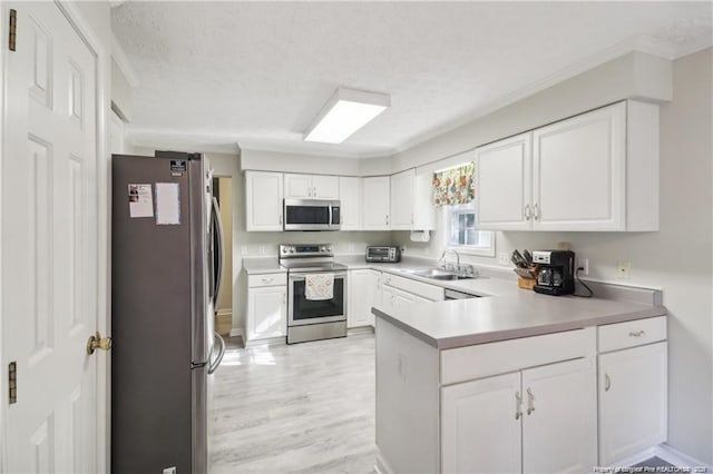 kitchen with a textured ceiling, stainless steel appliances, a peninsula, a sink, and white cabinetry