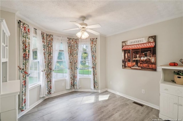 unfurnished dining area with ornamental molding, visible vents, a textured ceiling, and wood finished floors