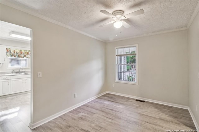 spare room with a sink, visible vents, a ceiling fan, ornamental molding, and light wood finished floors