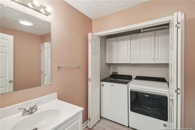 laundry area with a textured ceiling, independent washer and dryer, a sink, and cabinet space