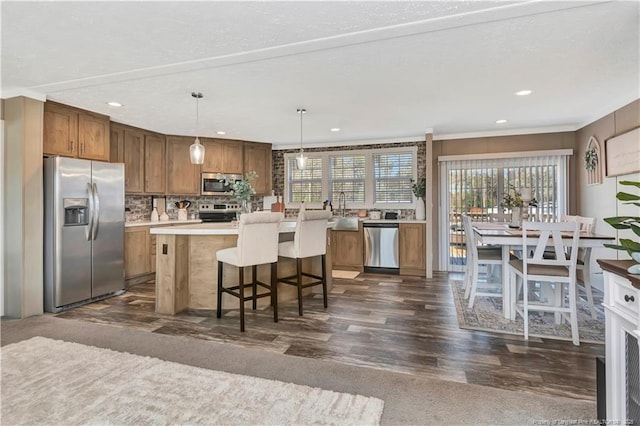 kitchen featuring stainless steel appliances, a kitchen island, light countertops, brown cabinets, and decorative light fixtures