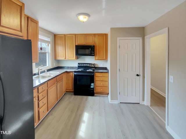 kitchen featuring light wood finished floors, baseboards, dark countertops, black appliances, and a sink