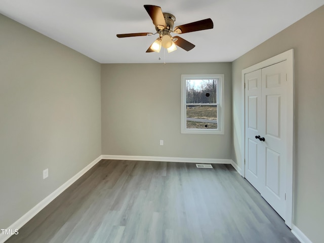 unfurnished bedroom featuring wood finished floors, visible vents, a ceiling fan, baseboards, and a closet