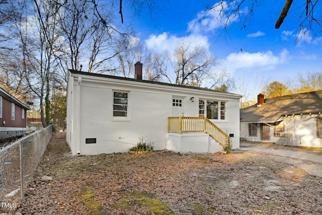 rear view of house featuring crawl space, a chimney, fence, and brick siding