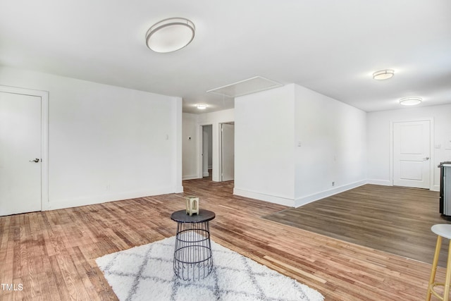 unfurnished living room with attic access, baseboards, and wood finished floors