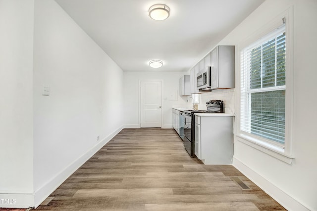 kitchen with baseboards, black electric range, light countertops, light wood finished floors, and stainless steel microwave