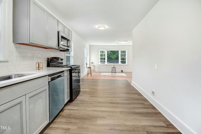 kitchen with light wood finished floors, stainless steel appliances, light countertops, decorative backsplash, and baseboards