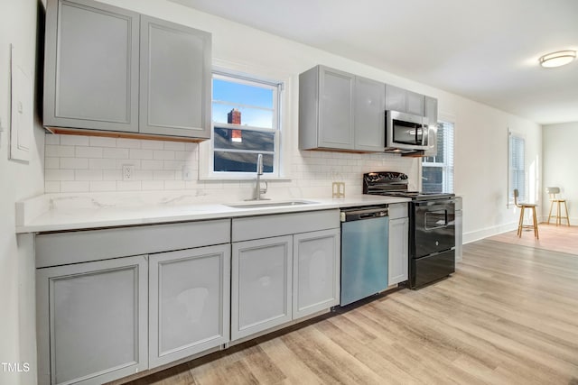 kitchen featuring tasteful backsplash, appliances with stainless steel finishes, gray cabinetry, light wood-style floors, and a sink