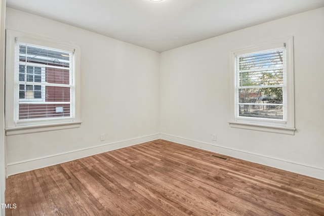 spare room featuring baseboards, visible vents, and wood finished floors