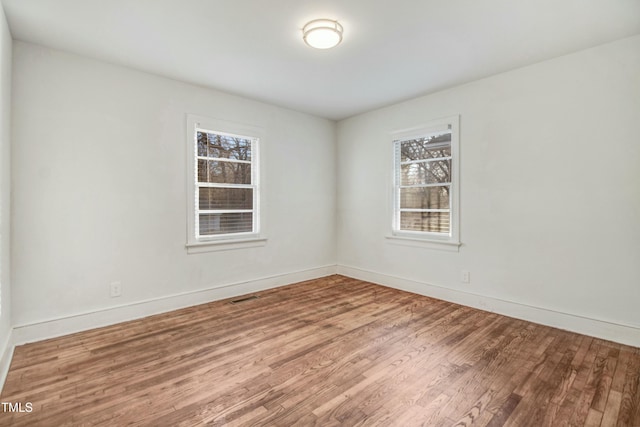 spare room with baseboards, visible vents, and wood finished floors