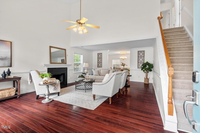 living area with a fireplace with flush hearth, ceiling fan with notable chandelier, stairs, and wood finished floors