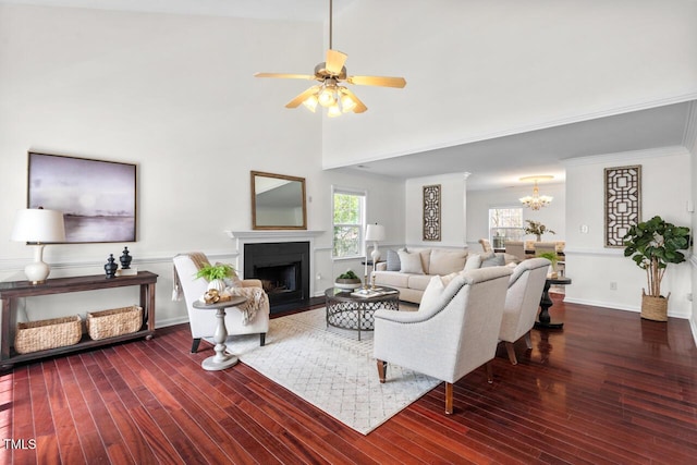 living area featuring ceiling fan with notable chandelier, a fireplace with flush hearth, wood finished floors, and baseboards