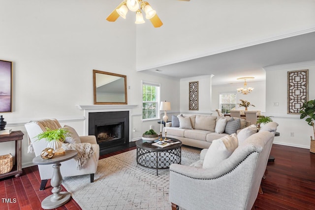 living room with a fireplace with flush hearth, ornamental molding, ceiling fan with notable chandelier, a towering ceiling, and wood-type flooring