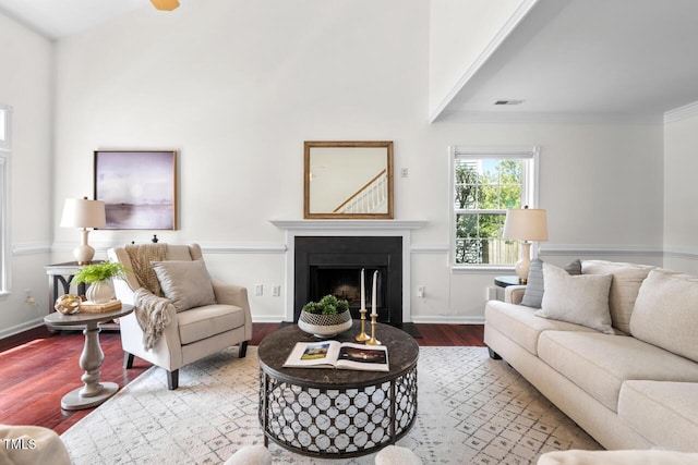 living area with wood finished floors, visible vents, baseboards, a fireplace, and crown molding