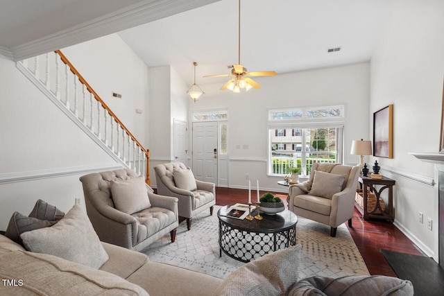 living area with wood finished floors, visible vents, a ceiling fan, a high ceiling, and stairs