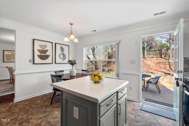 kitchen with ornamental molding, gray cabinetry, light countertops, stone finish floor, and a chandelier