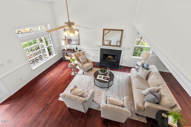 living area with wood finished floors, baseboards, a fireplace with flush hearth, ceiling fan, and a towering ceiling