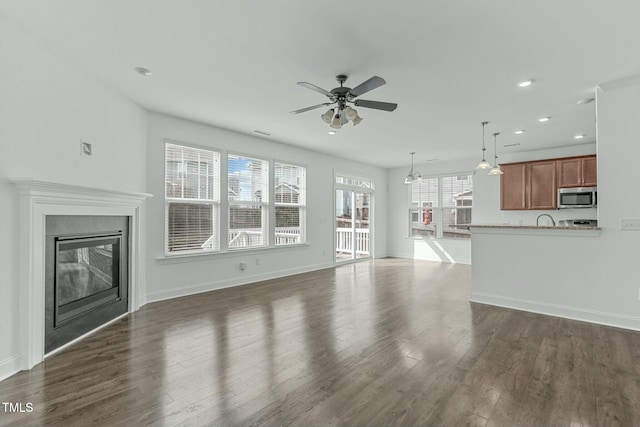 unfurnished living room featuring a glass covered fireplace, dark wood finished floors, baseboards, and ceiling fan