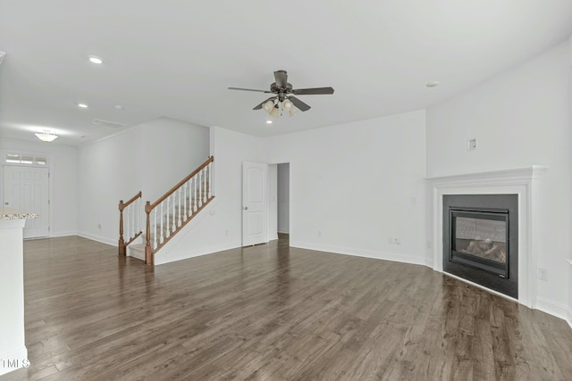 unfurnished living room with recessed lighting, stairway, dark wood-type flooring, a glass covered fireplace, and baseboards