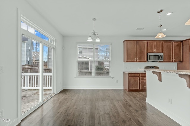 kitchen featuring a kitchen bar, stainless steel microwave, pendant lighting, and dark wood-style flooring