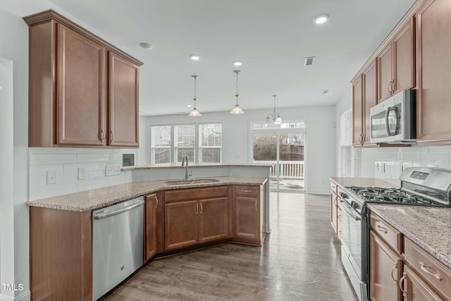 kitchen with light stone counters, light wood-style flooring, appliances with stainless steel finishes, a sink, and a peninsula