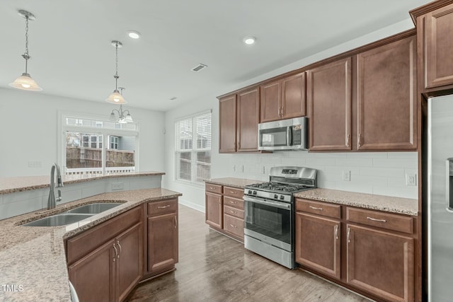 kitchen with light wood-style flooring, stainless steel appliances, a sink, visible vents, and tasteful backsplash