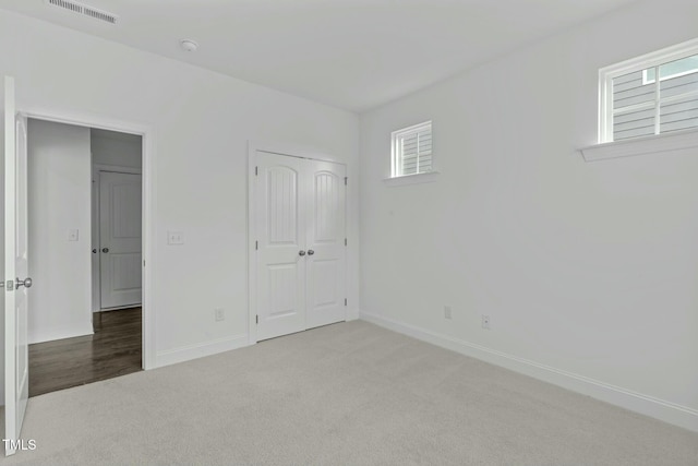 unfurnished bedroom featuring carpet floors, multiple windows, and visible vents