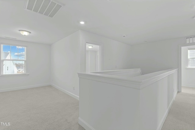 hallway with light carpet, plenty of natural light, visible vents, and an upstairs landing