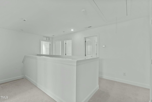 empty room with baseboards, visible vents, attic access, and light colored carpet