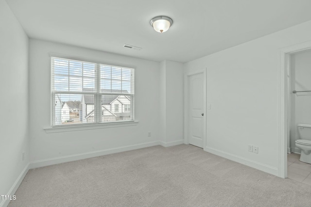 unfurnished bedroom featuring light colored carpet, visible vents, baseboards, and ensuite bathroom