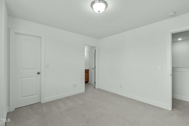 unfurnished bedroom featuring light carpet, a closet, ensuite bath, and baseboards