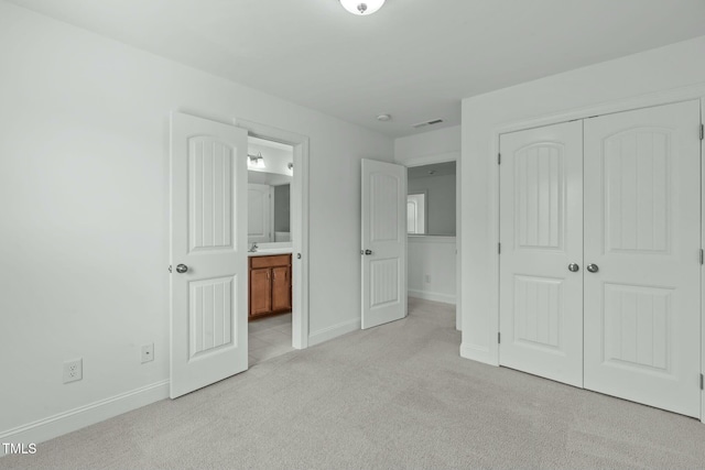 unfurnished bedroom featuring a closet, light colored carpet, connected bathroom, and baseboards