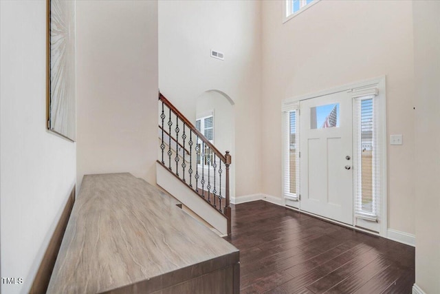 entrance foyer featuring visible vents, baseboards, stairway, wood finished floors, and a high ceiling