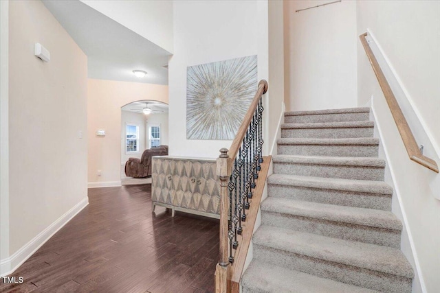 stairs featuring arched walkways, wood finished floors, and baseboards