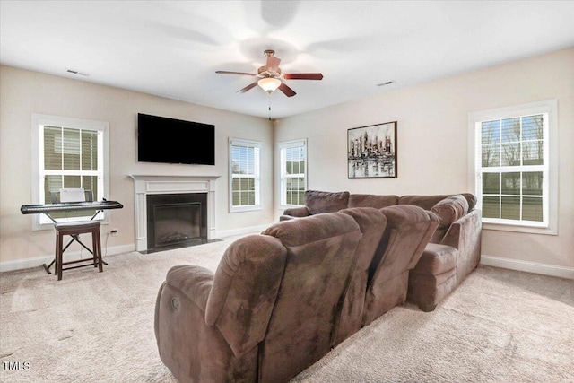 carpeted living area with baseboards, a fireplace with flush hearth, visible vents, and a ceiling fan