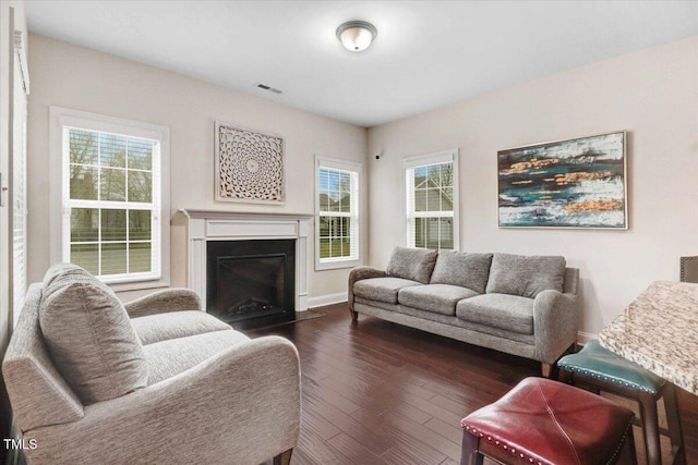 living area featuring dark wood-style floors, a fireplace with flush hearth, visible vents, and baseboards