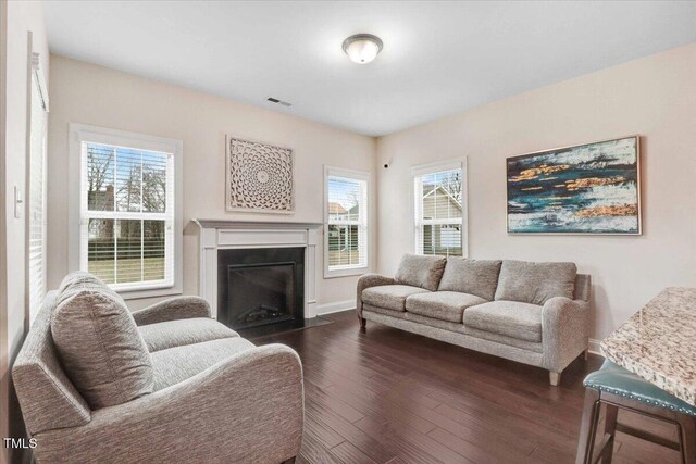 living area featuring dark wood-type flooring, a fireplace with flush hearth, visible vents, and baseboards