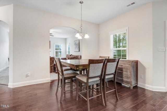 dining room featuring dark wood-style floors, arched walkways, visible vents, and baseboards