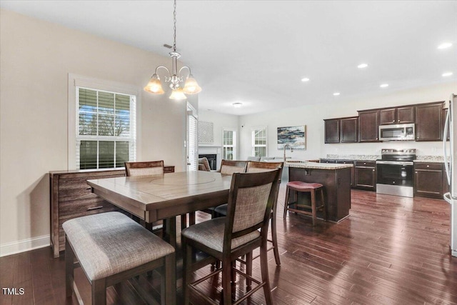 dining space with a notable chandelier, dark wood-style flooring, a fireplace, and recessed lighting