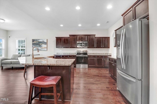 kitchen with appliances with stainless steel finishes, open floor plan, a sink, and dark wood-style floors