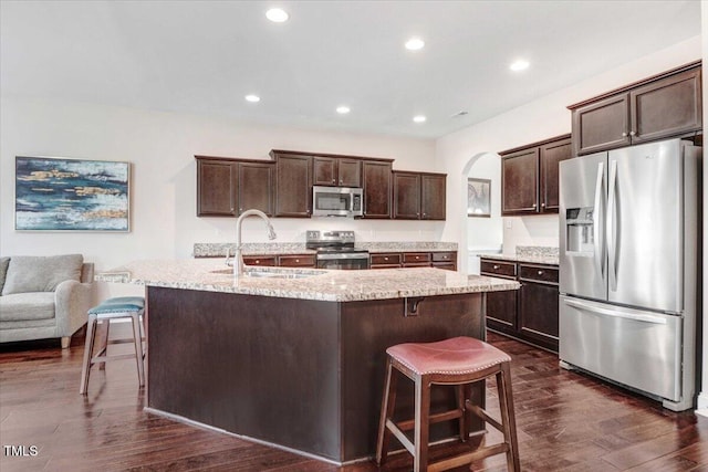 kitchen featuring dark wood finished floors, appliances with stainless steel finishes, a sink, dark brown cabinets, and a kitchen bar