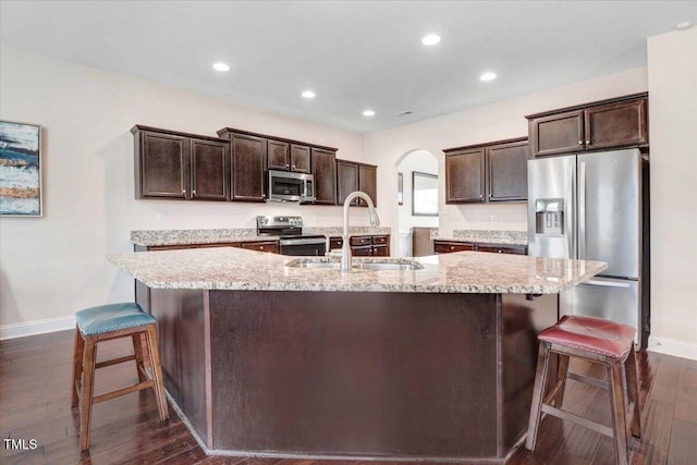 kitchen with appliances with stainless steel finishes, arched walkways, a sink, and dark brown cabinets